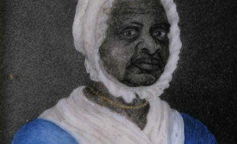 一个黑人妇女的肖像，她穿着一件蓝色的裙子，脖子和腰上系着细绳, 一条白色的围巾塞在她的裙子的脖子上, 一顶白帽子, 还有一条金串珠项链.