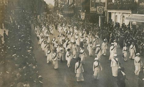 一些妇女在街上游行的黑白照片, 在人群的注视下，她穿着相配的白色套装，系着深色腰带